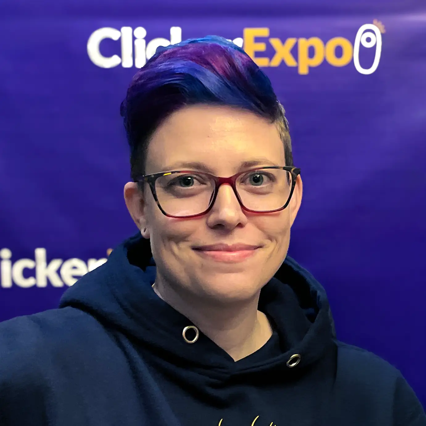 meet karen a person with glasses and purple hair stands in front of a purple clicker expo background